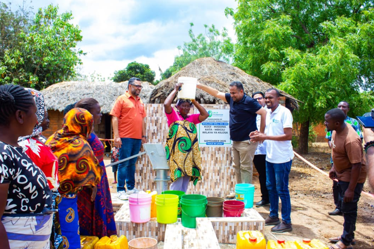 Lalji-foundation-chairman-helping-a-woman carry a bucket of water at mabana shallow well