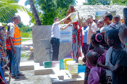 Lalji foundation representative helping a woman carry a water bucket at shallow well project